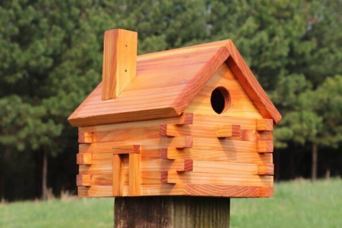 A wooden bird house standing on a wooden pole.