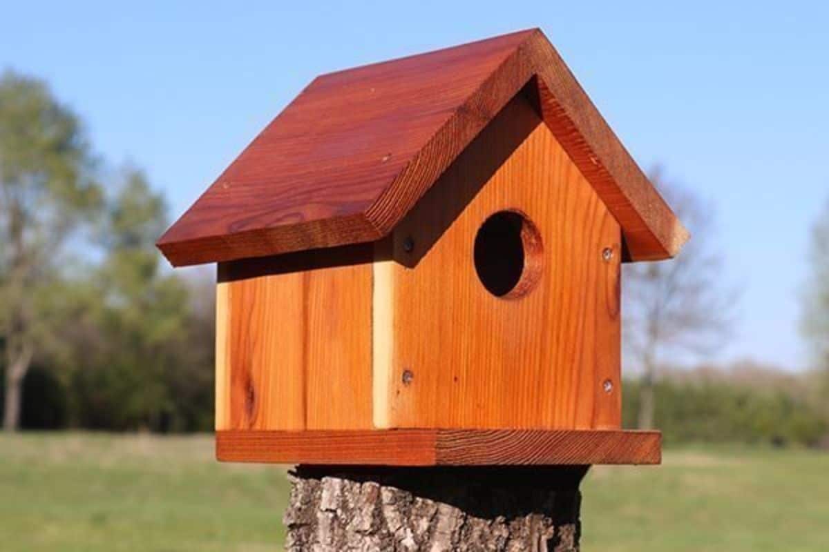 A wooden bird house on a wooden pole.